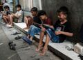 BEBERAPA kanak-kanak bermain permainan dalam talian menggunakan telefon pintar dan tablet di kawasan lorong di Jakarta.- AFP