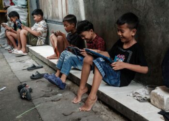 BEBERAPA kanak-kanak bermain permainan dalam talian menggunakan telefon pintar dan tablet di kawasan lorong di Jakarta.- AFP