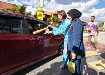 SANDREA NG menyampaikan bubur lambuk kepada pengguna jalan raya di Bulatan Sultan Azlan Shah di Meru Raya, Ipoh hari ini.