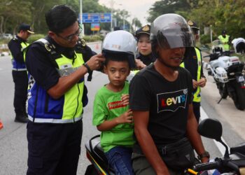 MOHD. Zamri Samion (kiri) memakaikan topi keledar baharu kepada pembonceng motosikal pada Majlis Penutup Op HRA dan Operasi Khas Motosikal peringkat negeri di Jalan Sultan Mohamad, Kuala Terengganu, Terengganu. -UTUSAN/PUQTRA HAIRRY