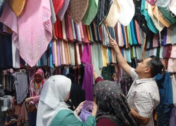 KHALIL Muhamad (kanan) melayan pelanggan membeli tudung di kedainya di Hentian Bas Majlis Bandaraya Kuala Terengganu (MBKT) Kuala Terengganu, Terengganu. – UTUSAN/ ERMA YUSNIDA JUSOH