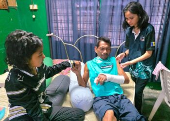 ZULKFLI Iham Abdul Majid yang patah tangan dijaga dua anaknya di Kampung Tersusun Padang Tembak di Teluk Intan, Perak. - UTUSAN/AIN SAFRE BIDIN