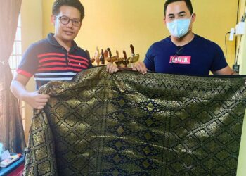 NIK Mohamad Salahudin Nik Nizam ( kanan) menunjukan samping tenun asli Terengganu kepada pelanggan.