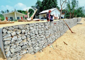SEORANG pekerja chalet Kampung Inn, Abdul Hadi Abdullah menunjukkan tembok gabion yang dibina di Pantai Cherating Lama di Kuantan, Pahang. – UTUSAN/SHAIKH AHMAD RAZIF