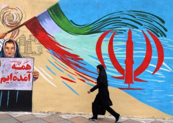 SEORANG wanita Iran berjalan melepasi mural anti AS dan Israel di Teheran.-AFP