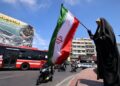 SEORANG wanita mengibarkan bendera kebangsaan Iran di hadapan papan iklan yang tertulis 'Selat Hormuz kekal ditutup' di Dataran Revolusi di Teheran.- AFP