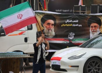 SEORANG budak lelaki mengibarkan bendera Iran di sebelah sepanduk memaparkan foto bekas pemimpin tertinggi Iran, Ayatollah Ali Khamenei dan Ayatollah Ali Sistani (kiri) semasa perhimpunan pro-Iran di Baghdad.- AFP
