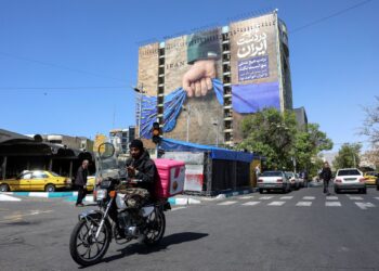 SEORANG lelaki menunggang motosikal melalui papan iklan besar yang merujuk kepada perang Iran dan Selat Hormuz di Dataran Vanak, Teheran.-AFP