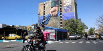 SEORANG lelaki menunggang motosikal melalui papan iklan besar yang merujuk kepada perang Iran dan Selat Hormuz di Dataran Vanak, Teheran.-AFP