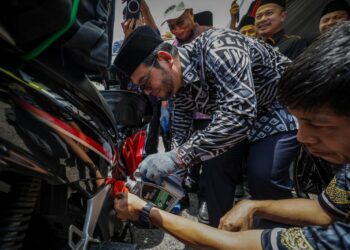 ZULKIFLI Hasan menuangkan minyak enjin pada salah sebuah motosikal p-hailing pada Majlis Ramah Mesra Pemandu E-hailing dan P-hailing Barakah Pit Stop di Masjid Wilayah Persekutuan, Kuala Lumpur. - UTUSAN/MUHAMAD IQBAL ROSLI
