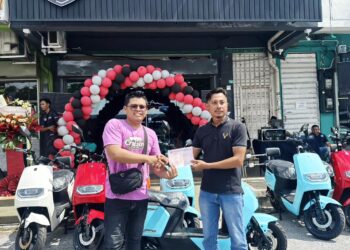 MOHAMED Izwan Abdul Karim (kanan) menyerahkan geran motosikal EV kepada pembeli pertama di GGR X EV Ipoh, Mohd Farhan Noh hari ini. - UTUSAN/LIYANA RAMLI