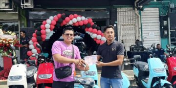 MOHAMED Izwan Abdul Karim (kanan) menyerahkan geran motosikal EV kepada pembeli pertama di GGR X EV Ipoh, Mohd Farhan Noh hari ini. - UTUSAN/LIYANA RAMLI