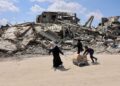 BEBERAPA orang berjalan dekat runtuhan bangunan di Gaza. - AFP