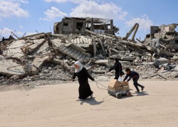 BEBERAPA orang berjalan dekat runtuhan bangunan di Gaza. - AFP