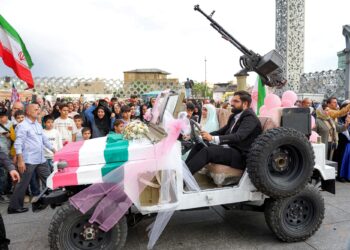 PASANGAN pengantin menaiki jip tentera ketika tiba untuk majlis perkahwinan beramai-ramai di Dataran Imam Hossein di Teheran, Iran.-AFP