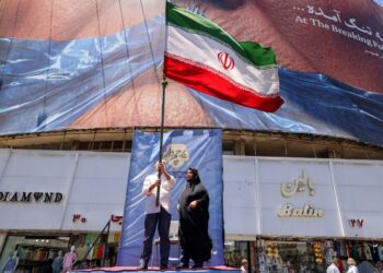 SEORANG lelaki mengibarkan bendera kebangsaan Iran ketika berdiri di hadapan iklan politik yang memaparkan Presiden AS, Donald Trump dan Selat Hormuz di Dataran Valiasr di Teheran.- AFP