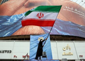 SEORANG wanita mengibarkan bendera Iran di hadapan papan iklan anti-Amerika yang merujuk kepada Presiden Donald Trump dan Selat Hormuz di Dataran Valiasr di Teheran.- AFP