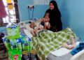 NUR Izzati Farhana Sazali memangku anak sulungnya sambil melihat keadaan Wan Mohd. Amzar Wan Ahmad yang koma di Kampung Lati, Pasir Mas, Kelantan.