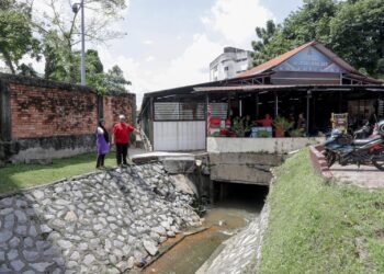 JAMALIAH Yusoff (kiri) bersama Idris Shah Mahmud menunjukkan longkang yang dinaiki air akibat banjir kilat susulan hujan lebat berterusan di Medan Selera Jaya, Petaling Jaya, Selangor. - UTUSAN/FARIZ RUSADIO