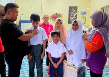 MOHD. Nazari Sabran (kiri) memakaikan baju sekolah kepada tiga beradik yang akan memulakan persekolahan tidak lama lagi di Langkap di Pasir Salak, Perak. - UTUSAN/AIN SAFRE BIDIN