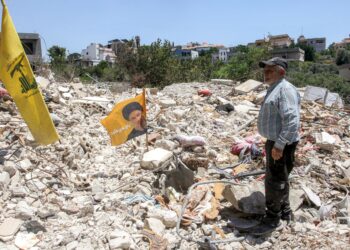ALI Hassan Najdi  berdiri berhampiran bendera Hizbullah di celah runtuhan rumah sepupunya, tempat 13 anggota keluarganya terbunuh dalam serangan Israel di Deir Qanoun al-Nahr. - AFP