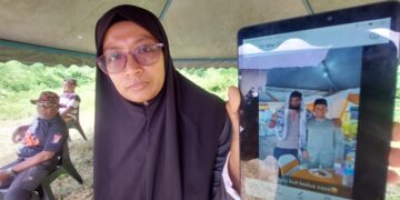 NORMAZITA Ishury menunjukkan gambar Samsul Azmi (kiri dalam gambar) yang hilang dikhuatiri lemas di Sungai Pahang dekat Kampung Peragap di Temerloh, Pahang.