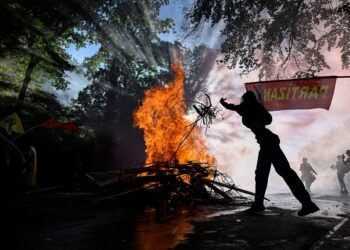 SEORANG penunjuk perasaan membaling rating ke dalam api di Geneva. - AFP