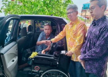 RAJA Nurshirwan Zainal Abidin menyerahkan kerusi roda kepada seorang penerima di pekarangan Wat Machimmaram Jubakar Tumpat, Kelantan. - UTUSAN/ ROHANA ISMAIL