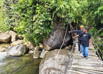NAZRI Bah Eng (belakang) dan Bah Roslan menunjukkan lokasi mereka memancing ketika melihat kehadiran Jaslinda Saludin yang melalui jambatan gantung di Kampung Lubuk Gaharu, Pos Musuh, Tapah.