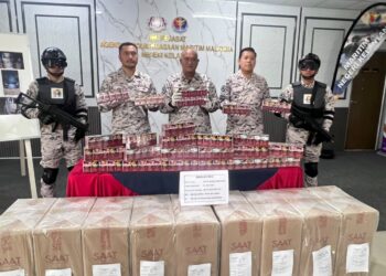 KAMAL Mohamad (tengah) menunjukkan rokok seludup yang dirampas dalam serbuan di Kampung Penambang, Kota Bharu, Kelantan.