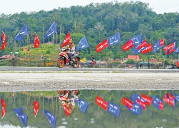 WANITA bersama anaknya menunggang motosikal berlatar belakangkan deretan bendera parti politik yang menghiasi perkampungan di Seri Menanti, Kuala Pilah, semalam. – UTUSAN/ISKANDAR ISHAK