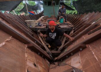 PEMBUAT bot, Borhanuddin Syafie (kanan) dan Muhammad Pirdaus Ismail (kiri) melakukan kerja-kerja memasang komponen bot tradisional di Pulau Duyung, Kuala Terengganu, Terengganu.  
– UTUSAN/PUQTRA HAIRRY