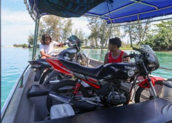 MUHAMMAD Syukor Adam Che Wahab (kiri) dan Mohd. Irwan Rosman mengangkut motosikal Yamaha RXZ menggunakan bot dari Pulau Redang menuju ke Program RXZ Members 8.0 di Gong Badak, Terengganu. – UTUSAN/PUQTRA HAIRRY