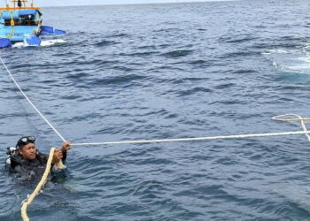Mohd Amirul Mat Noh (kiri) menaikkan bot candat sotong yang karam di kedalaman 24 meter di dasar laut kira-kira lima batu nautika dari perairan Kuala Terengganu di sini semalam.