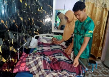 MUHAMMAD Nur Irfan Ab. Ghani (kanan) bersama Zubaidah Abdullah menguruskan Ab. Ghani A. Rahman yang terlantar akibat strok di Kampung Gong Ubi Keling, Besut, Terengganu. – UTUSAN/WAN ZURATIKAH IFFAH WAN ZULKIFLI
