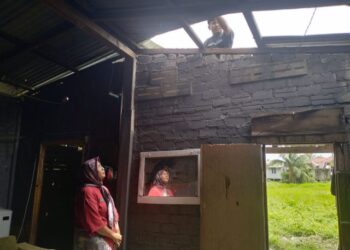 SITI Norfadhilah Che Hashim melihat anak saudaranya menggantikan zink yang tercabut di Kampung Kok Serai, Tumpat, Kelantan, semalam. - UTUSAN/ ROHANA ISMAIL