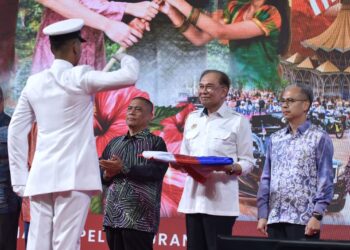 ANWAR Ibrahim menyerahkan Jalur Gemilang kepada Bintara Kanan TLDM, Mohamad Razif Aliff Md. Yusof untuk upacara mengibar Jalur Gemilang pada Majlis Peluncuran Bulan Kebangsaan dan Kibar Jalur Gemilang 2026 di Ipoh hari ini. - UTUSAN/ZULFACHRI ZULKIFLI