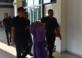TERTUDUH (tengah) diiringi polis semasa menghadiri prosiding perbicaraan di Mahkamah Seksyen Pasir Mas, Kelantan. - UTUSAN/ROSMIZAN RESDI