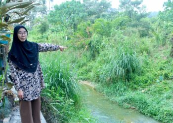 ROGAYAH Abdul Rani menunjukkan aliran air parit yang dipercayai mengalir dari kawasan tanah persendirian sehingga menyebabkan sungai di belakang rumahnya berbau busuk di Kampung Kayu Ara, Mambau, Seremban, Negeri Sembilan, semalam. – UTUSAN/NOR SHAFIQAH MOHD. GHAZALI