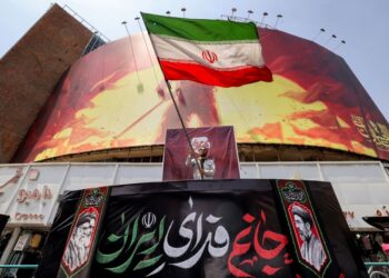 SEORANG lelaki mengibarkan bendera Iran di hadapan papan iklan di Dataran Valiasr di tengah Teheran.- AFP
