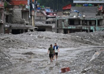 DUA lelaki berjalan selepas banjir dahsyat di daerah Nuwakot. - AFP