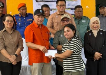 HAJIJI Noor menyampaikan bantuan kepada salah seorang mangsa kebakaran bertempat di Pusat Pemindahan Sementara (PPS) Dewan Serbaguna Likas. - UTUSAN/RAEESAH HANAN