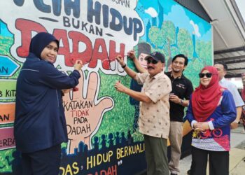 ROSLIN Jusoh (tengah) mewarna dinding yang dilukis bertemakan bebas dadah pada Majlis Sekolah Angkat Madani di Felda Tenang, Besut, Terengganu. UTUSAN / WAN ZURATIKAH IFFAH WAN ZULKIFLI
