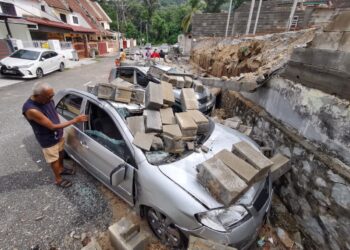SEORANG penduduk melihat kereta yang rosak dihempap tembok pagar yang sedang dibina dalam kejadian di Taman Jayamas, Seremban hari ini.-UTUSAN/MOHD. SHAHJEHAN MAAMIN.