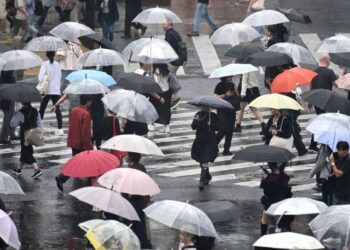 PEJALAN kaki membawa payung ketika melintasi jalan dalam hujan di daerah Shibuya, Tokyo.-AFP