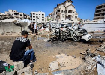 SEORANG lelaki duduk berhampiran sebuah kenderaan yang musnah susulan serangan Israel di kawasan kejiranan Rimal, Gaza. - AFP