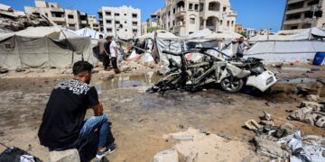 SEORANG lelaki duduk berhampiran sebuah kenderaan yang musnah susulan serangan Israel di kawasan kejiranan Rimal, Gaza. - AFP