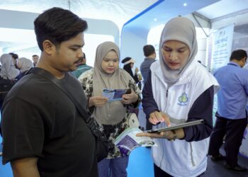 KAKITANGAN Pertubuhan Keselamatan Sosial (PERKESO), Che Nur Suhana Che Su (kanan) memberi penerangan kepada orang ramai yang hadir ke kaunter  Skim LINDUNG 24 Jam pada Festival Mega iLINDUNGu di Strand Mall di sini hari ini. - UTUSAN/FARIZ RUSADIO