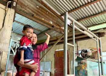 MARIATI Antek mendukung salah seorang anaknya, Muhammad Nazim Irfan sambil menunjukkan bahagian dapur rumah mereka yang bocor di Kampung Kuala Kangkong, Alor Setar, Kedah.