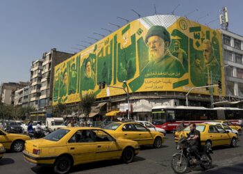 PENDUDUK melalui kawasan jalan raya yang sibuk melepasi sebuah papan iklan memaparkan gambar pemimpin yang terkorban di Teheran, Iran.-AFP